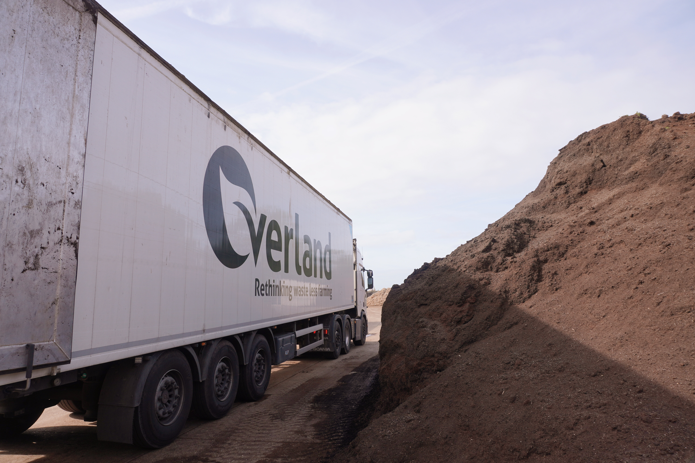 Overland lorry parked beside large piles of processed coir growing media